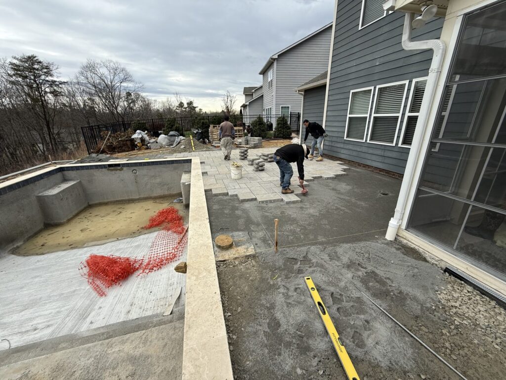 Crew laying a paver patio next to a pool